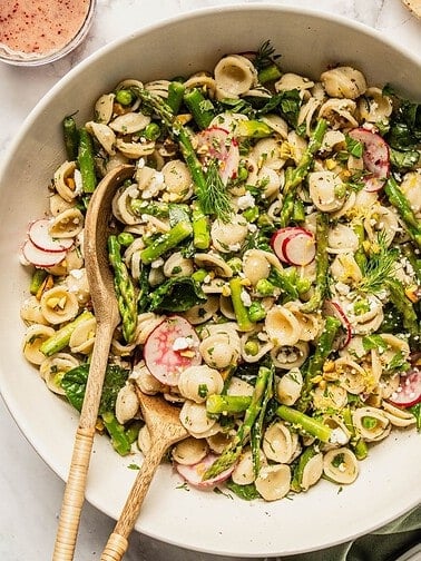 Spring pasta salad with asparagus and peas in a bowl with salad spoons.