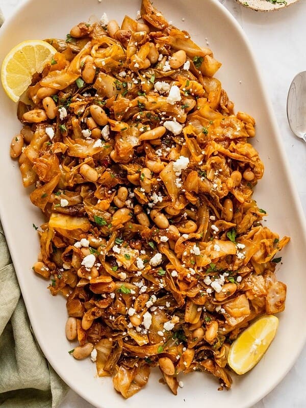 Delicious grilled chicken with beans, vegetables, and lemon wedges on a white platter.