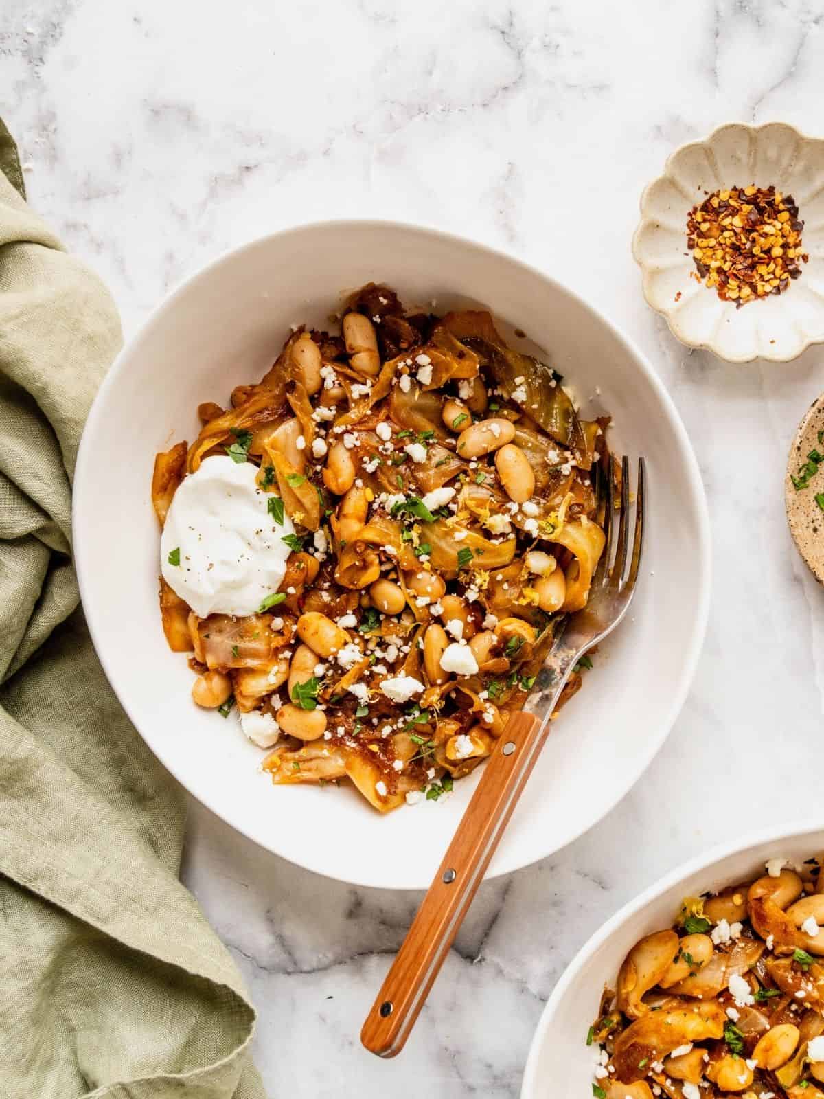 Plate of braised cabbage with white beans garnished with feta, yogurt, parsley and lemon.