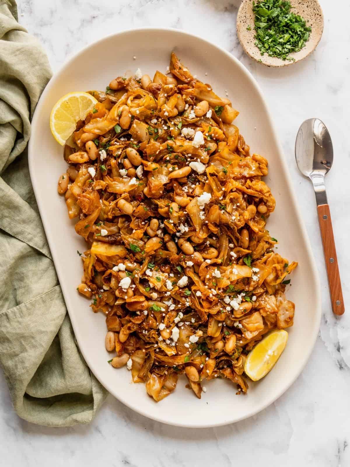 Platter of braised cabbage with white beans garnished with feta, parsley and lemon.