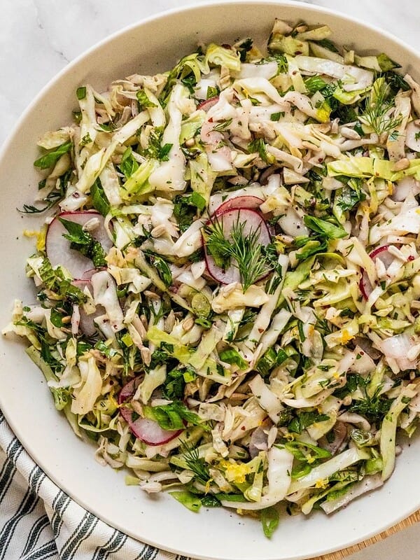 No mayo coleslaw with radish, fresh herbs in a lemon sumac dressing in a bowl.