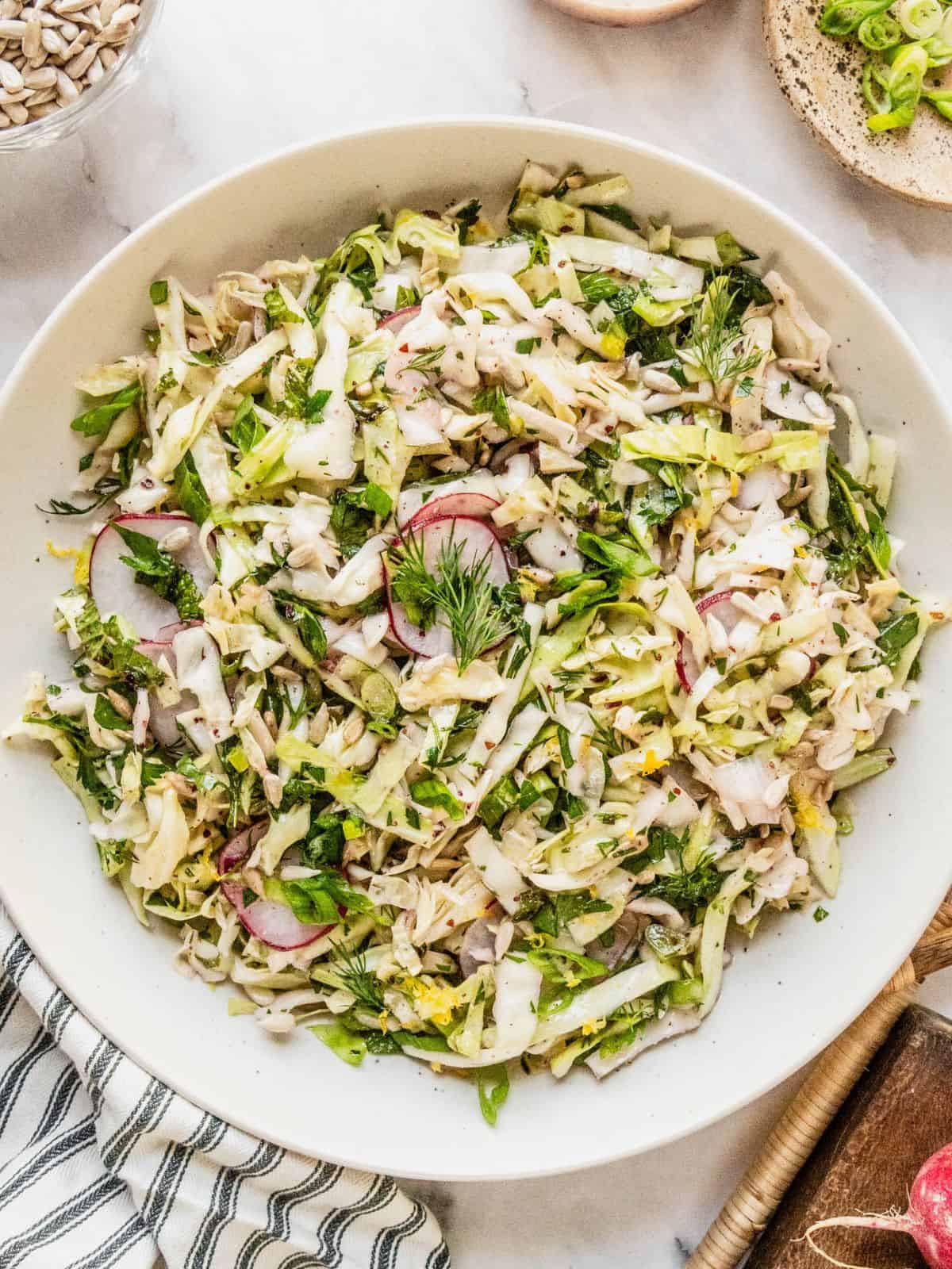 No mayo coleslaw with radish, fresh herbs in a lemon sumac dressing in a bowl.