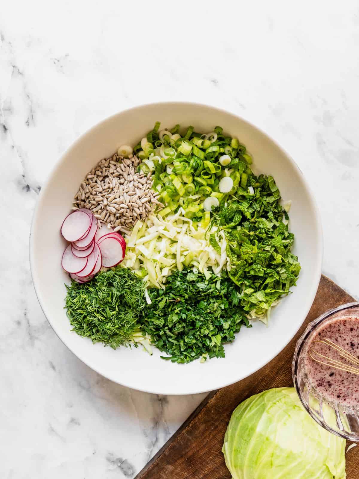 Large salad bowl with shredded cabbage, sliced radish, sunflower seeds and fresh herbs.