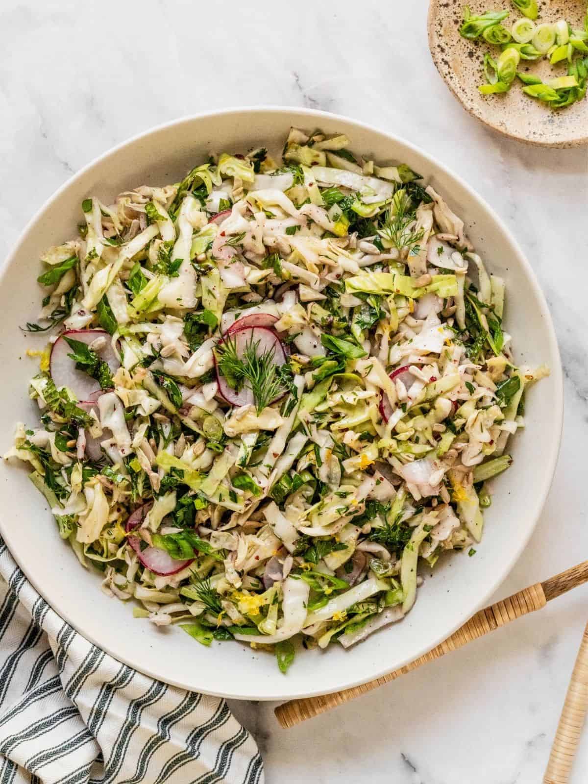 No mayo coleslaw with radish, fresh herbs in a lemon sumac dressing in a bowl.