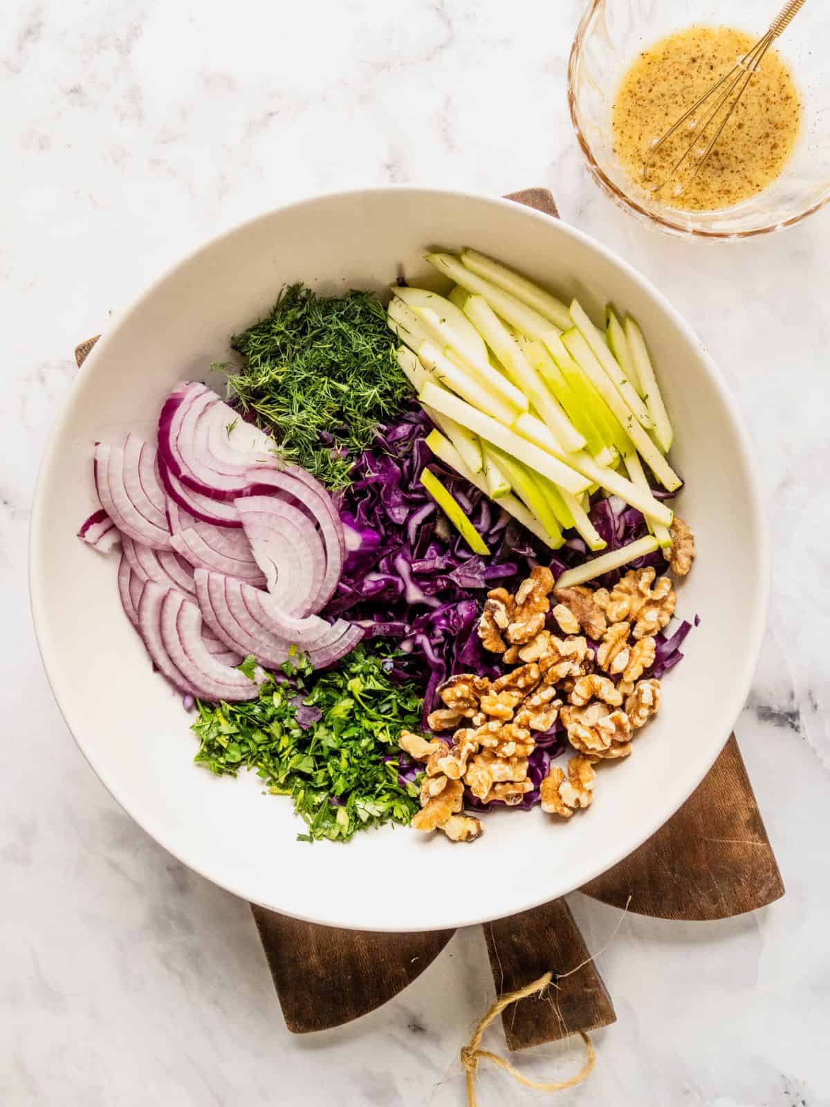 Bowl with sliced red cabbage, apples, onions, herbs and walnuts.