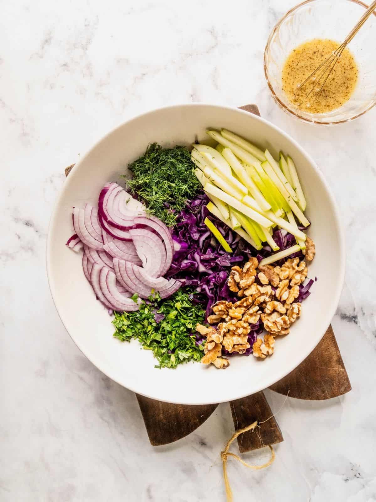 Bowl with sliced red cabbage, apples, onions, herbs and walnuts.