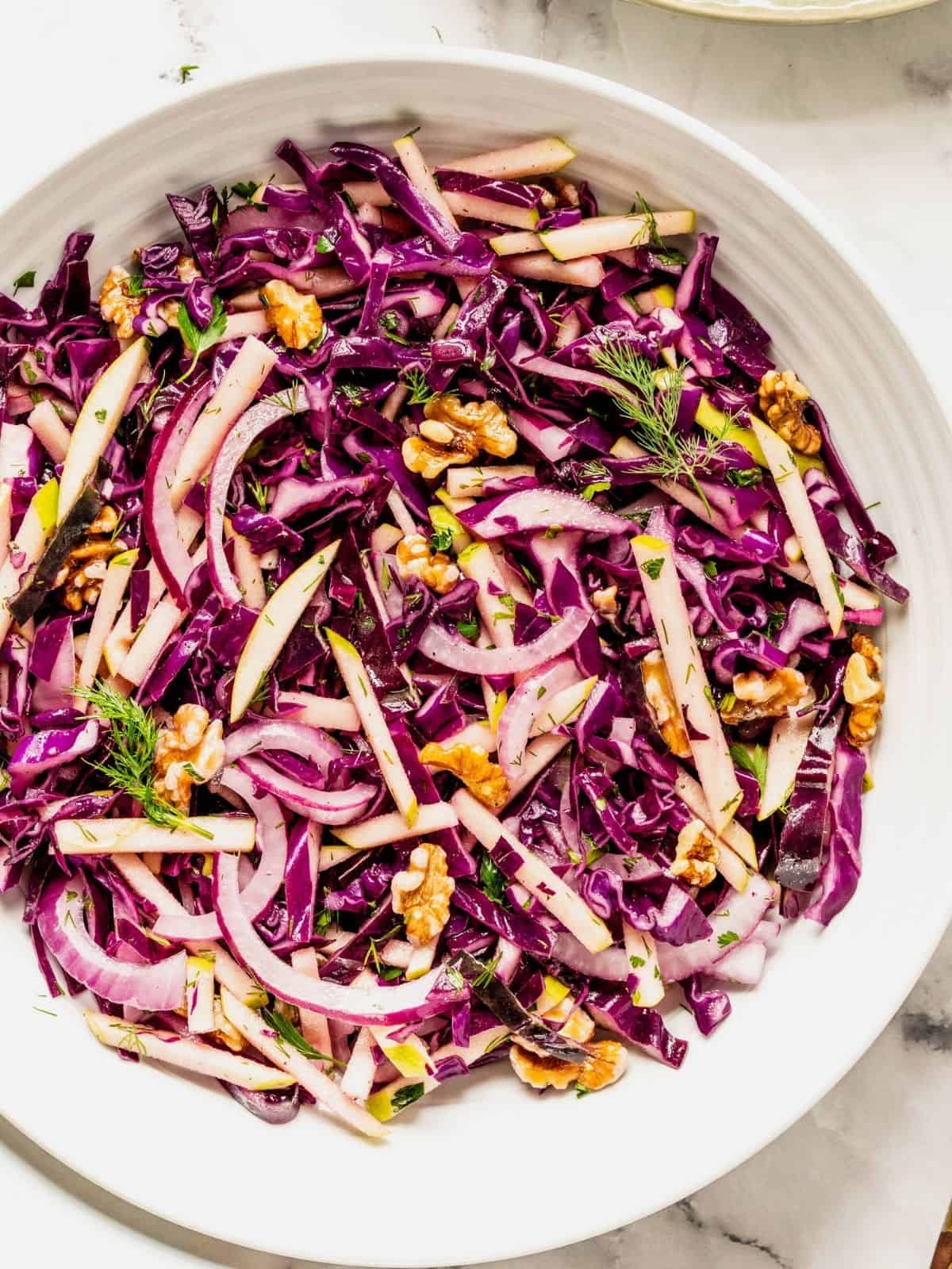 Purple cabbage slaw with apples and walnuts in a bowl.