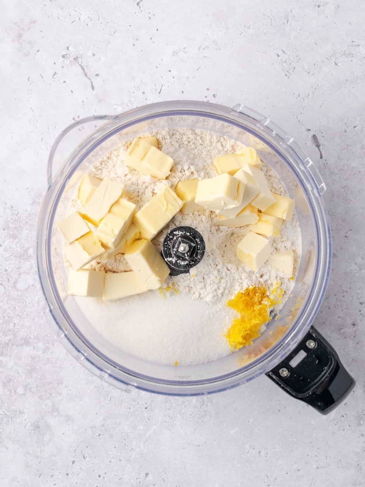 Food processor with flour, sugar, butter, lemon zest, baking soda and salt.