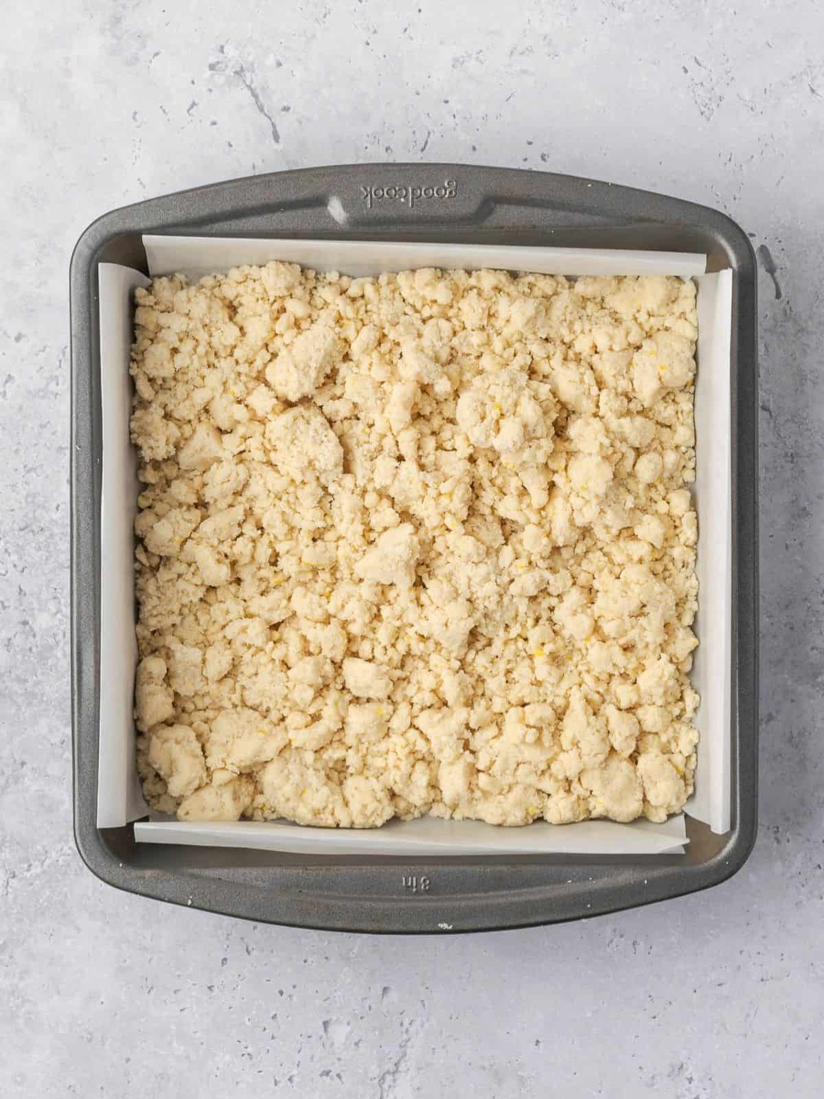The dough mixture getting added to a parchment paper lined metal square baking dish.