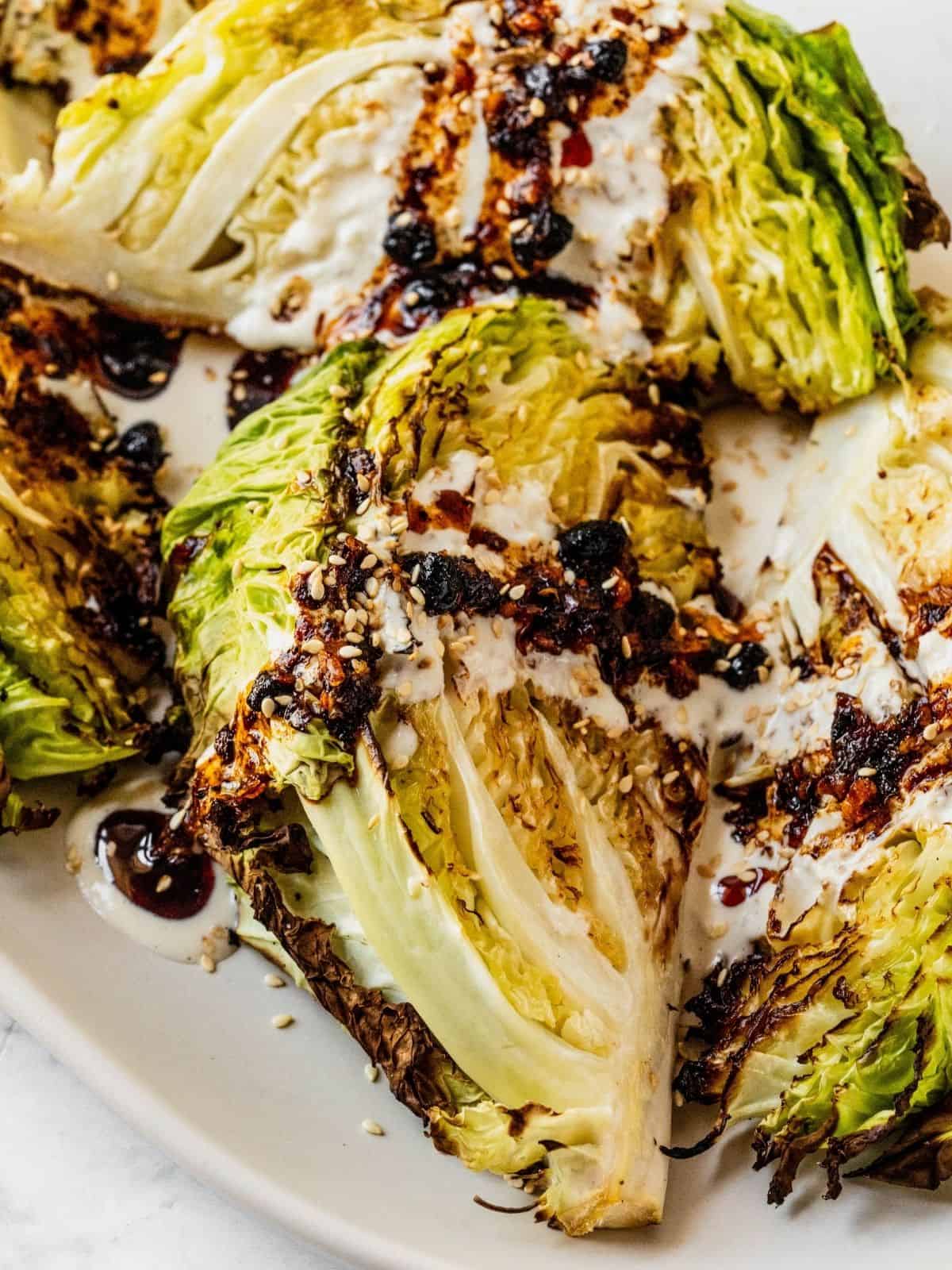 Roasted cabbage wedges with tahini and chili crisp drizzle on a serving platter.