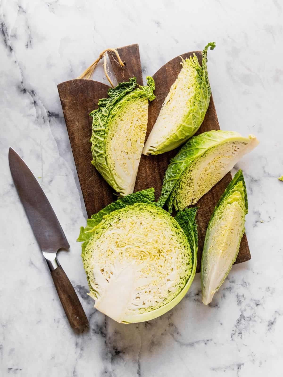 Savoy cabbage getting sliced into wedges on a wooden cutting board.