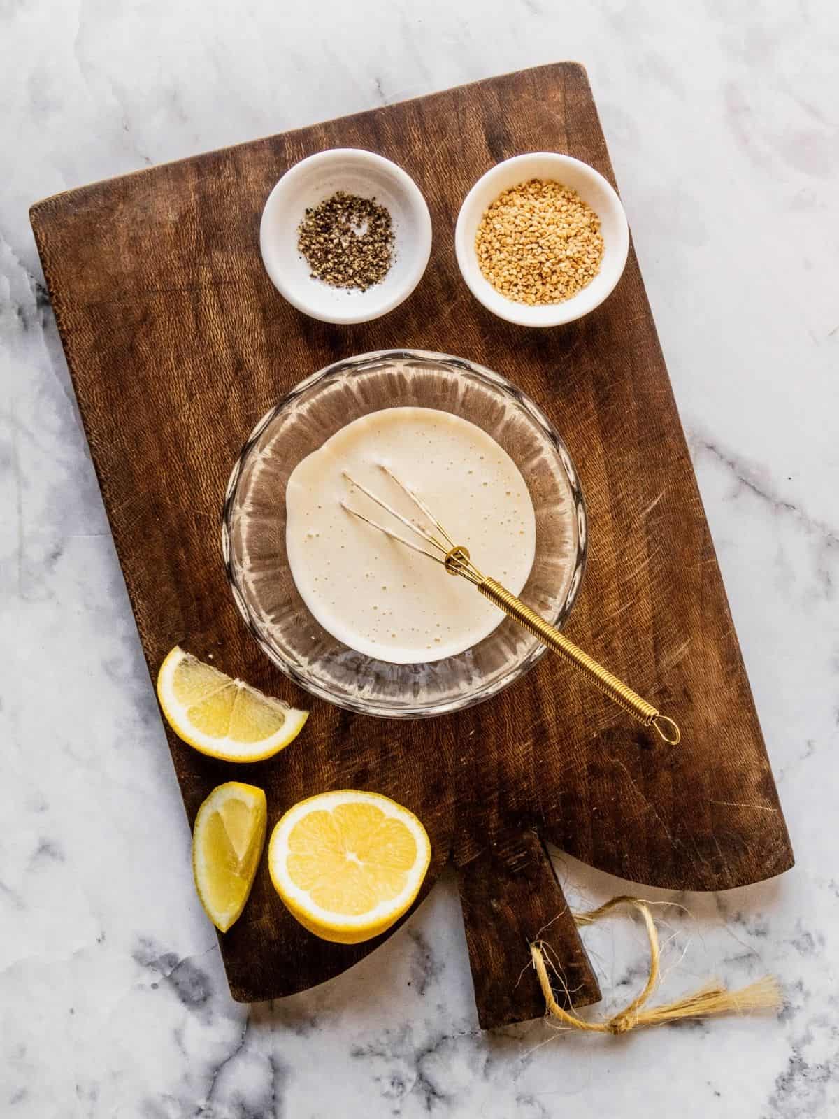Tahini lemon sauce getting whisked in a small bowl.