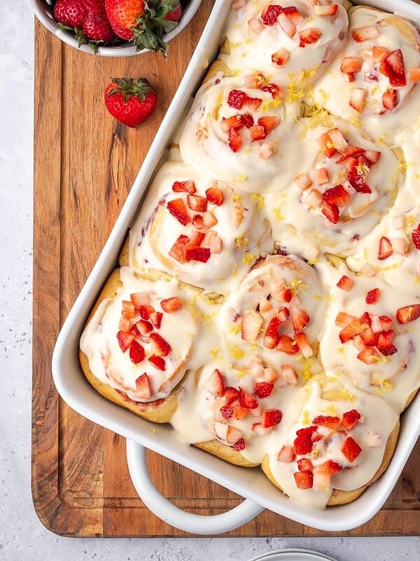 A tray of strawberry cinnamon rolls garnished with cream cheese icing and chopped strawberries.
