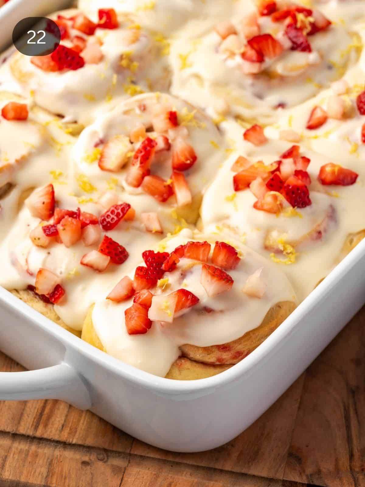 A tray of strawberry cinnamon rolls garnished with cream cheese icing and chopped strawberries.