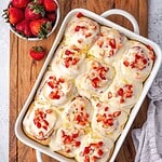 A tray of strawberry cinnamon rolls garnished with cream cheese icing and chopped strawberries.