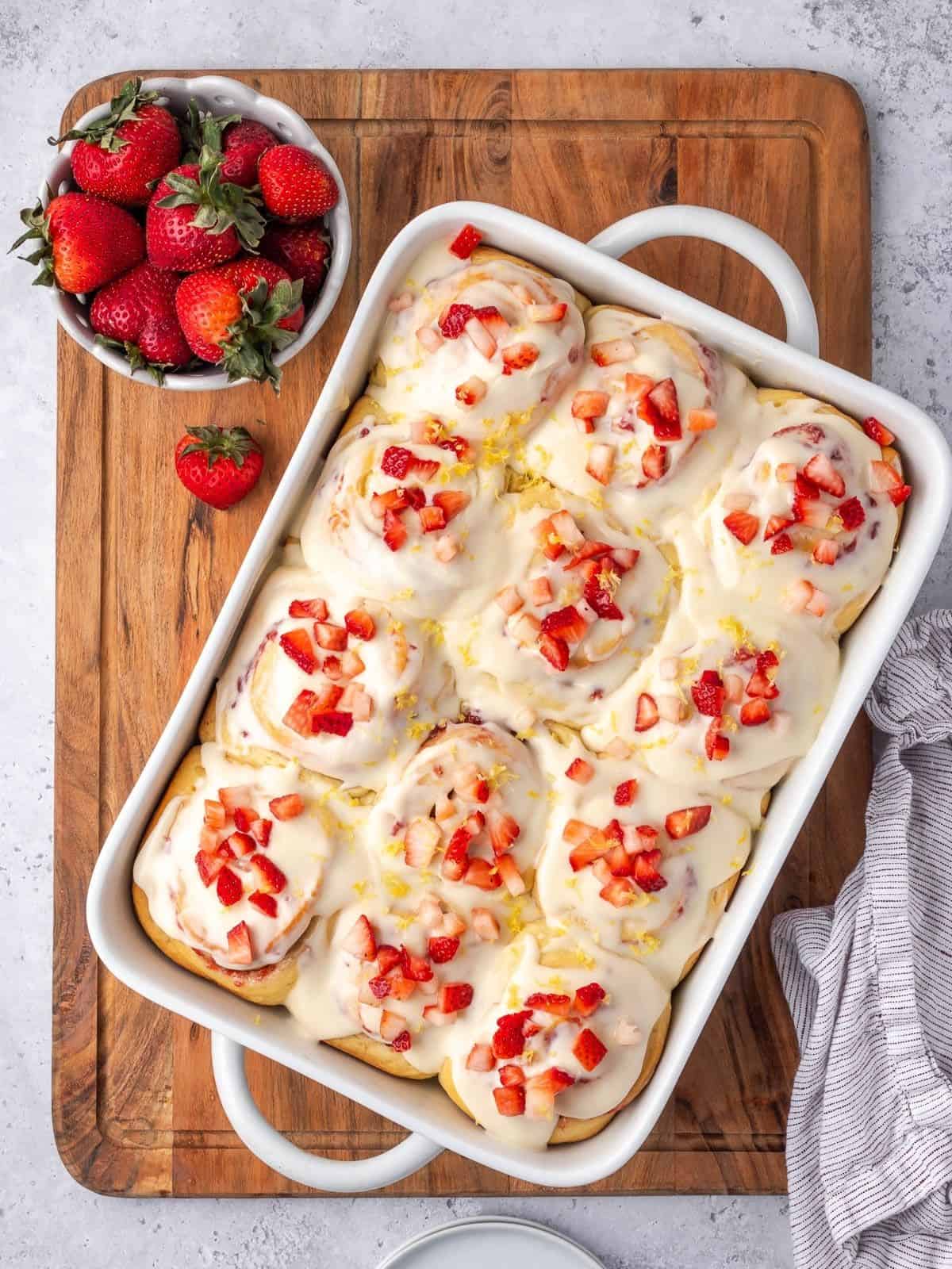 A tray of strawberry cinnamon rolls garnished with cream cheese icing and chopped strawberries.