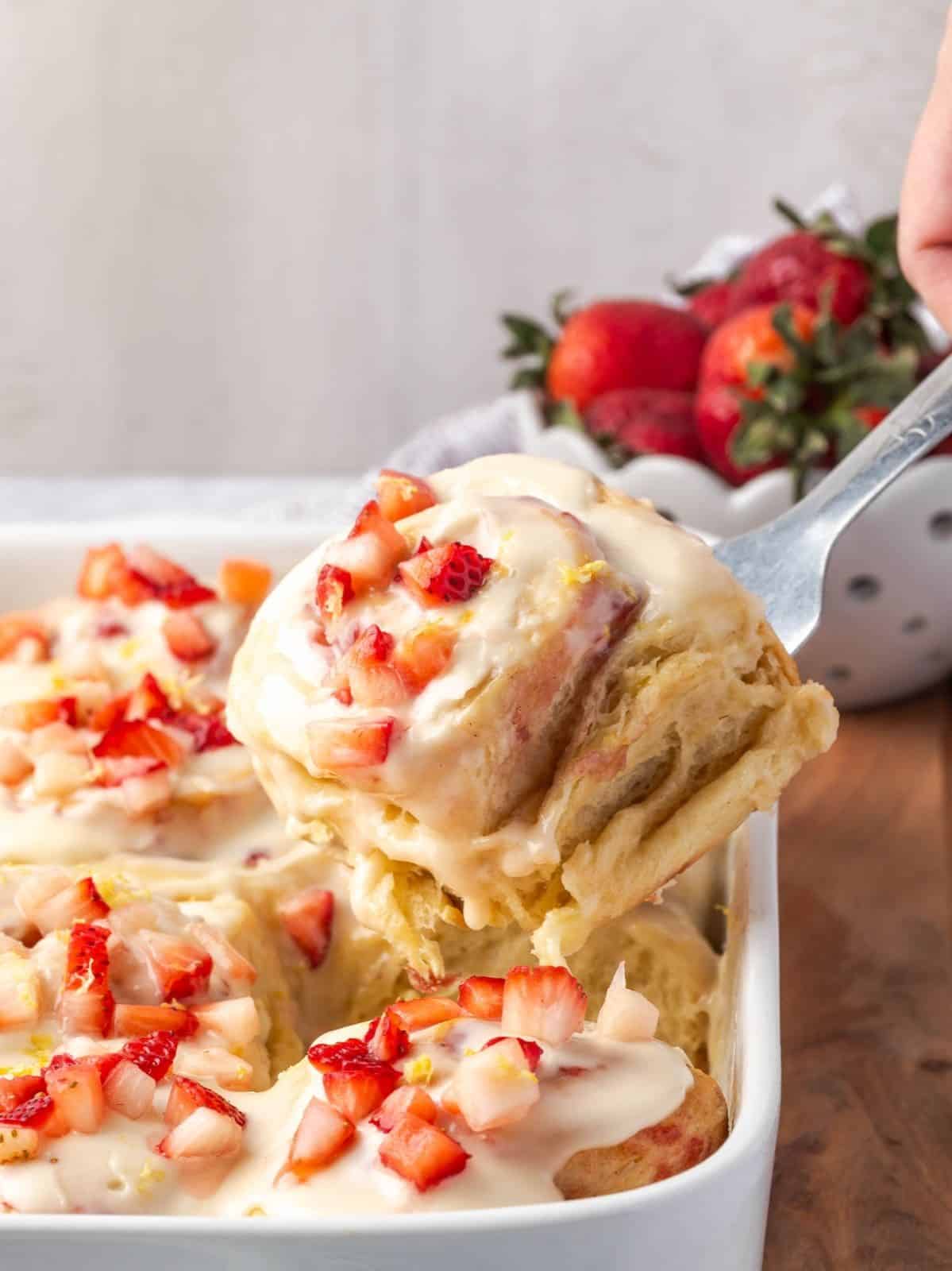 A tray of strawberry cinnamon rolls garnished with cream cheese icing and chopped strawberries.