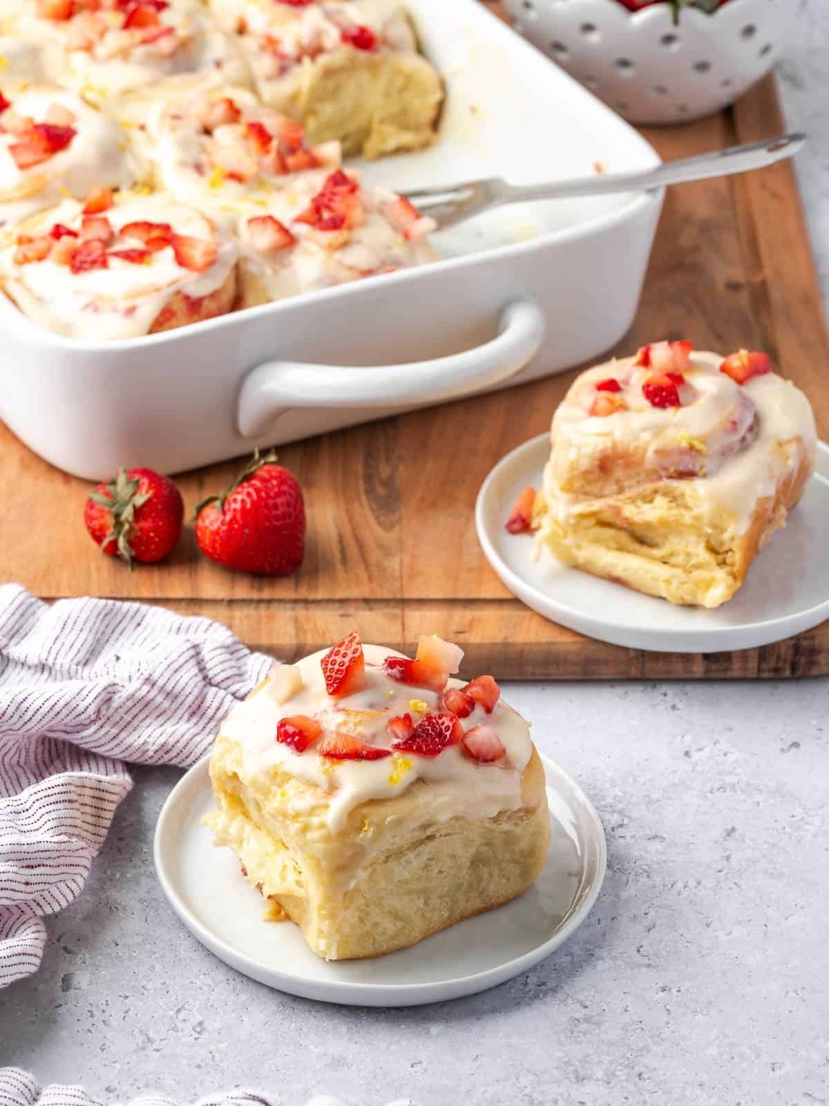 Strawberry cinnamon rolls garnished with cream cheese icing and chopped strawberries on plates.