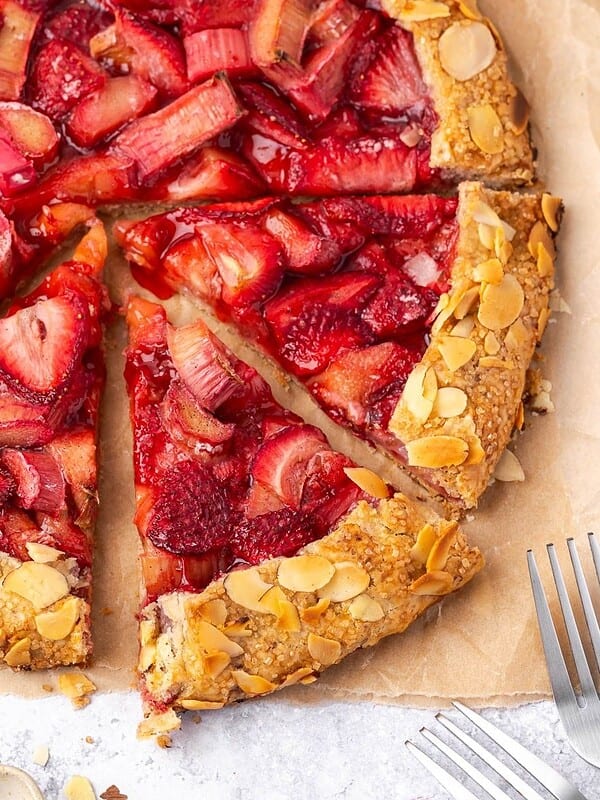 Sliced strawberry rhubarb galette with almond crust on parchment paper.