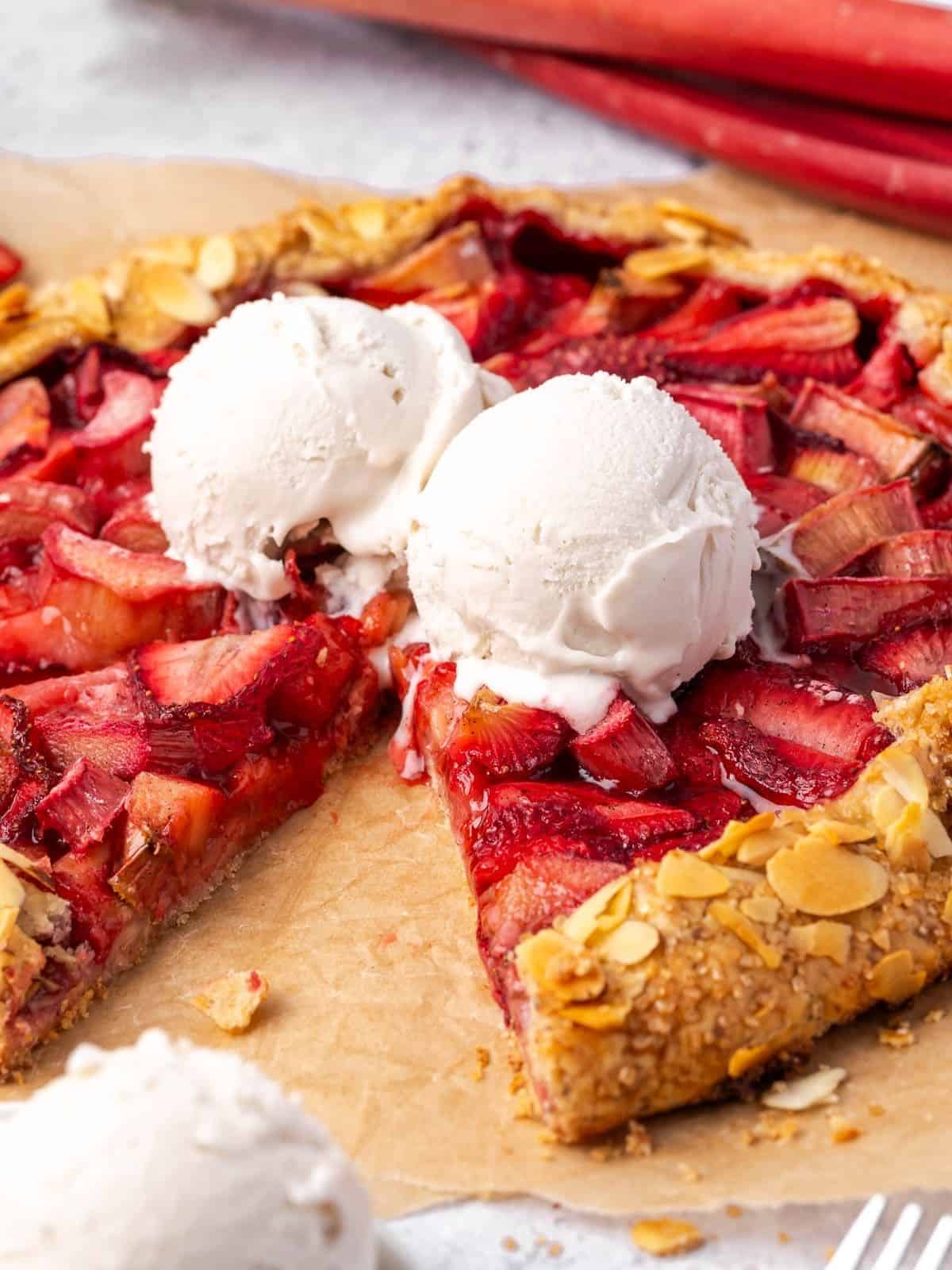 Two scoops of vanilla ice cream on top of sliced strawberry rhubarb almond galette.