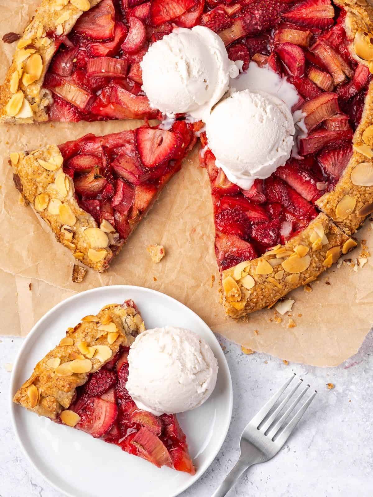 A plate with a slice of strawberry rhubarb galette and an ice cream scoop.