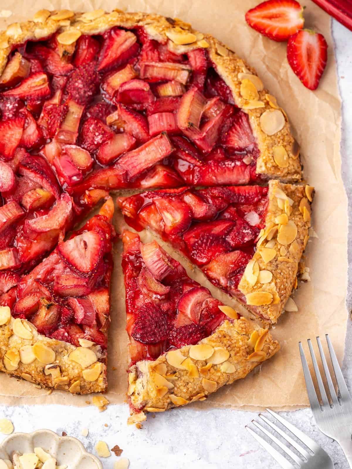 Sliced strawberry rhubarb galette with almond crust on parchment paper.