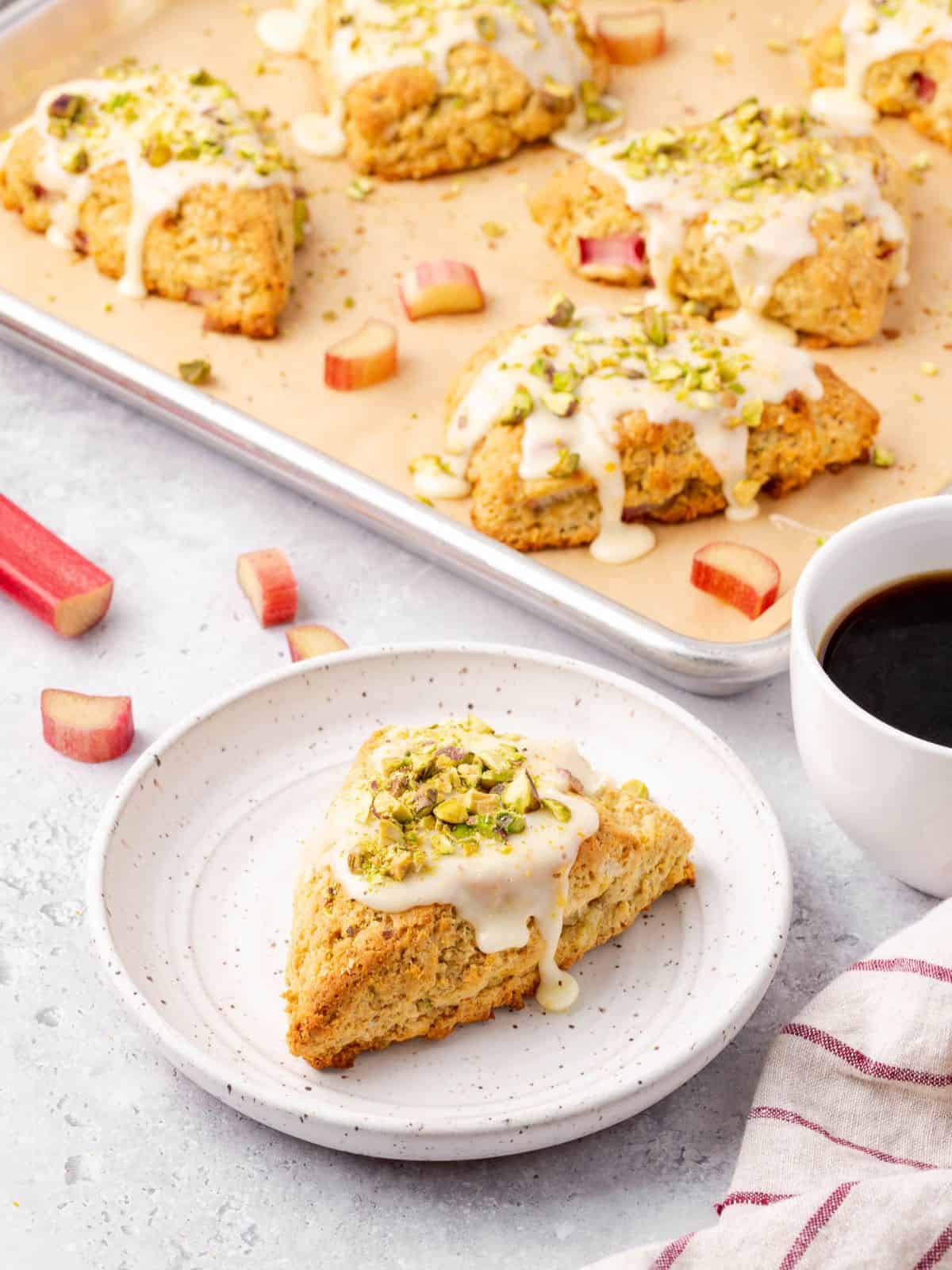 Rhubarb scone with orange glaze and pistachios on a plate with a side of black coffee.