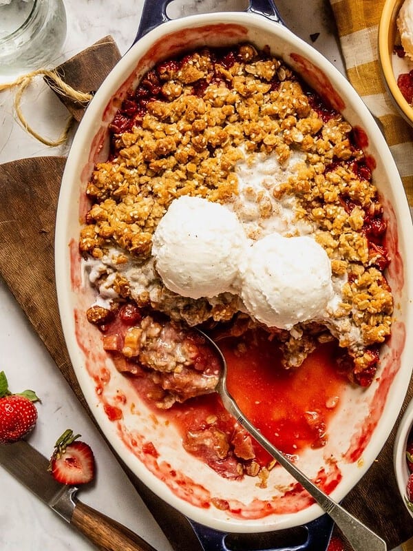 Strawberry rhubarb crisp with a tahini sesame topping in an oval dish with 2 scoops of ice cream.
