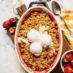 Strawberry rhubarb crisp with a tahini sesame topping in an oval dish with 3 scoops of ice cream.