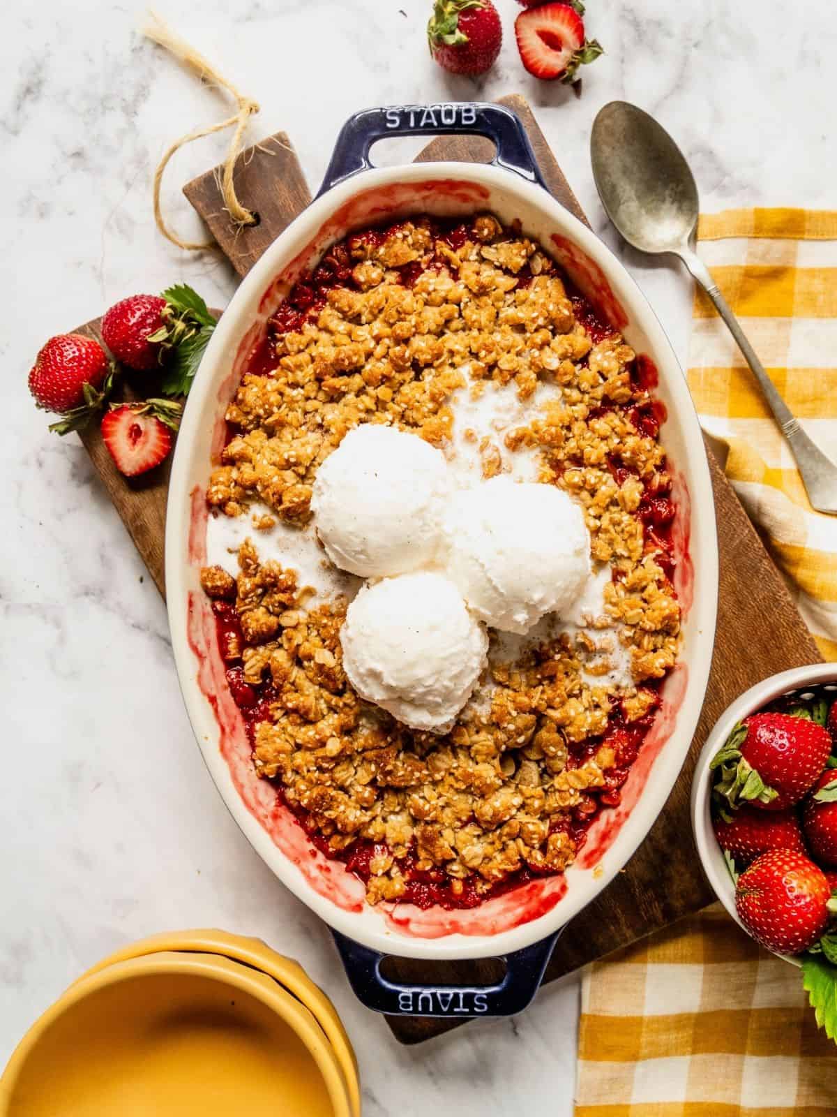Strawberry rhubarb crisp with a tahini sesame topping in an oval dish with 3 scoops of ice cream.