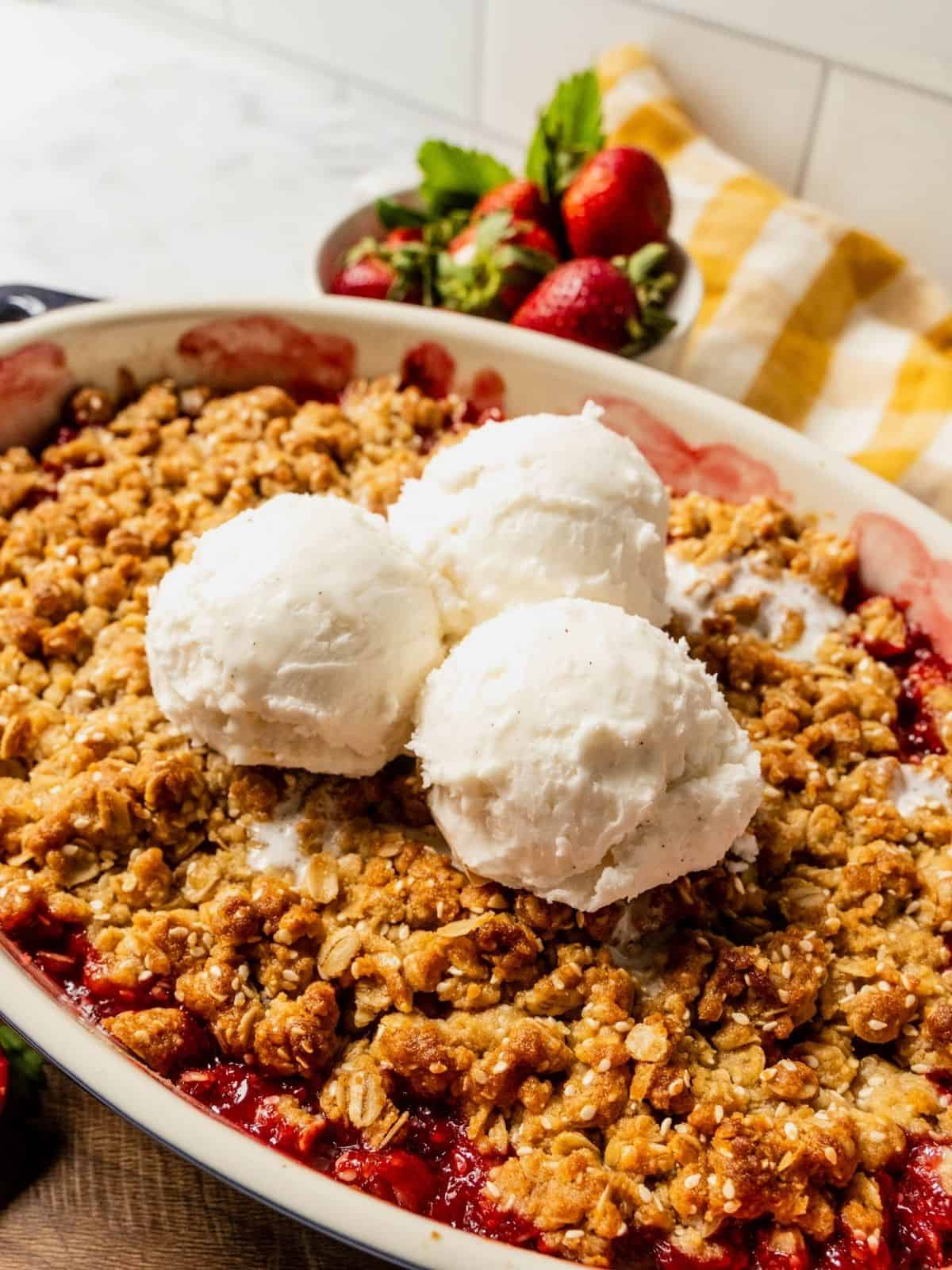 Strawberry rhubarb crisp with a tahini sesame topping in an oval dish with 3 scoops of ice cream.