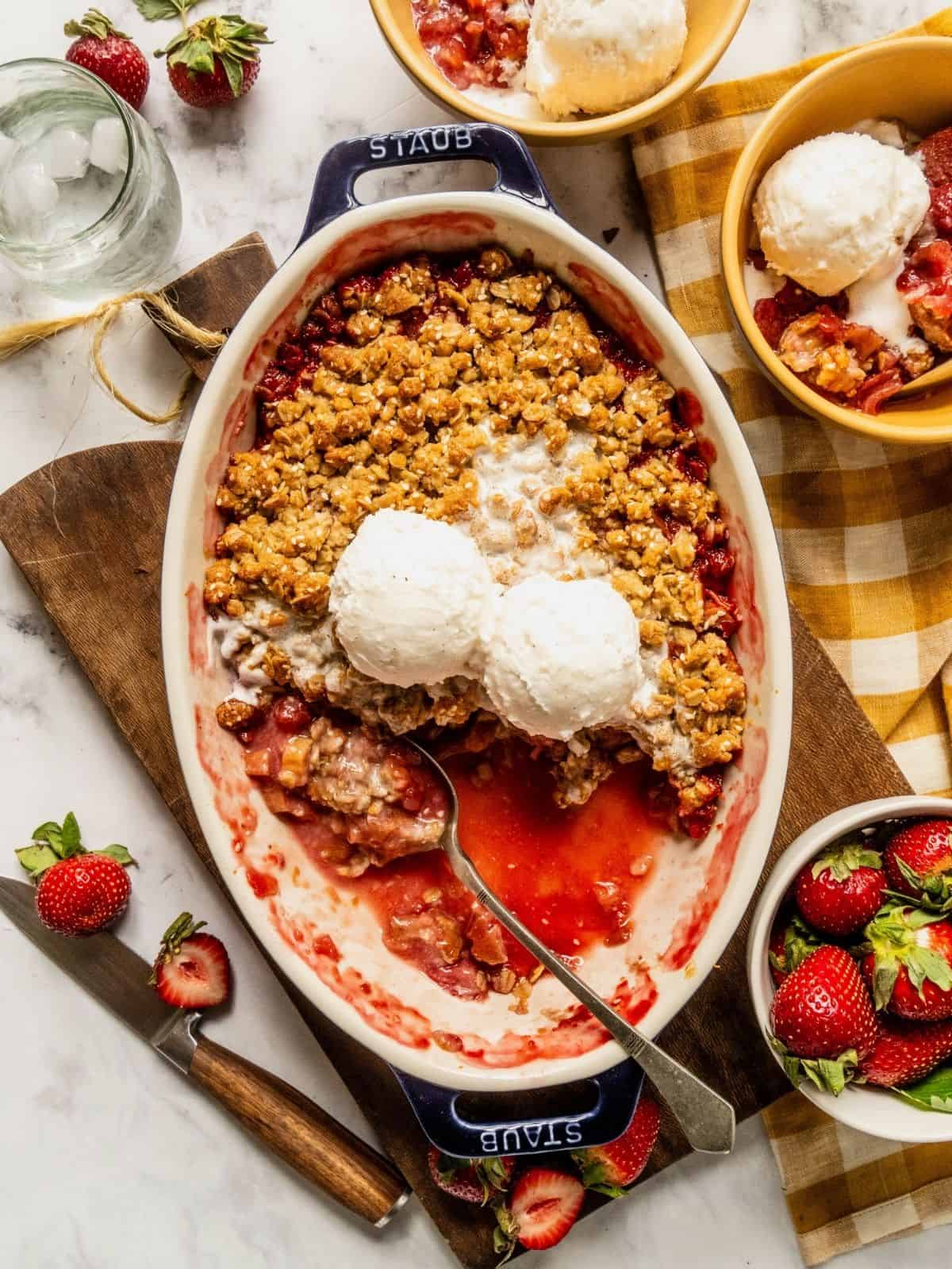Strawberry rhubarb crisp with a tahini sesame topping in an oval dish with 2 scoops of ice cream.