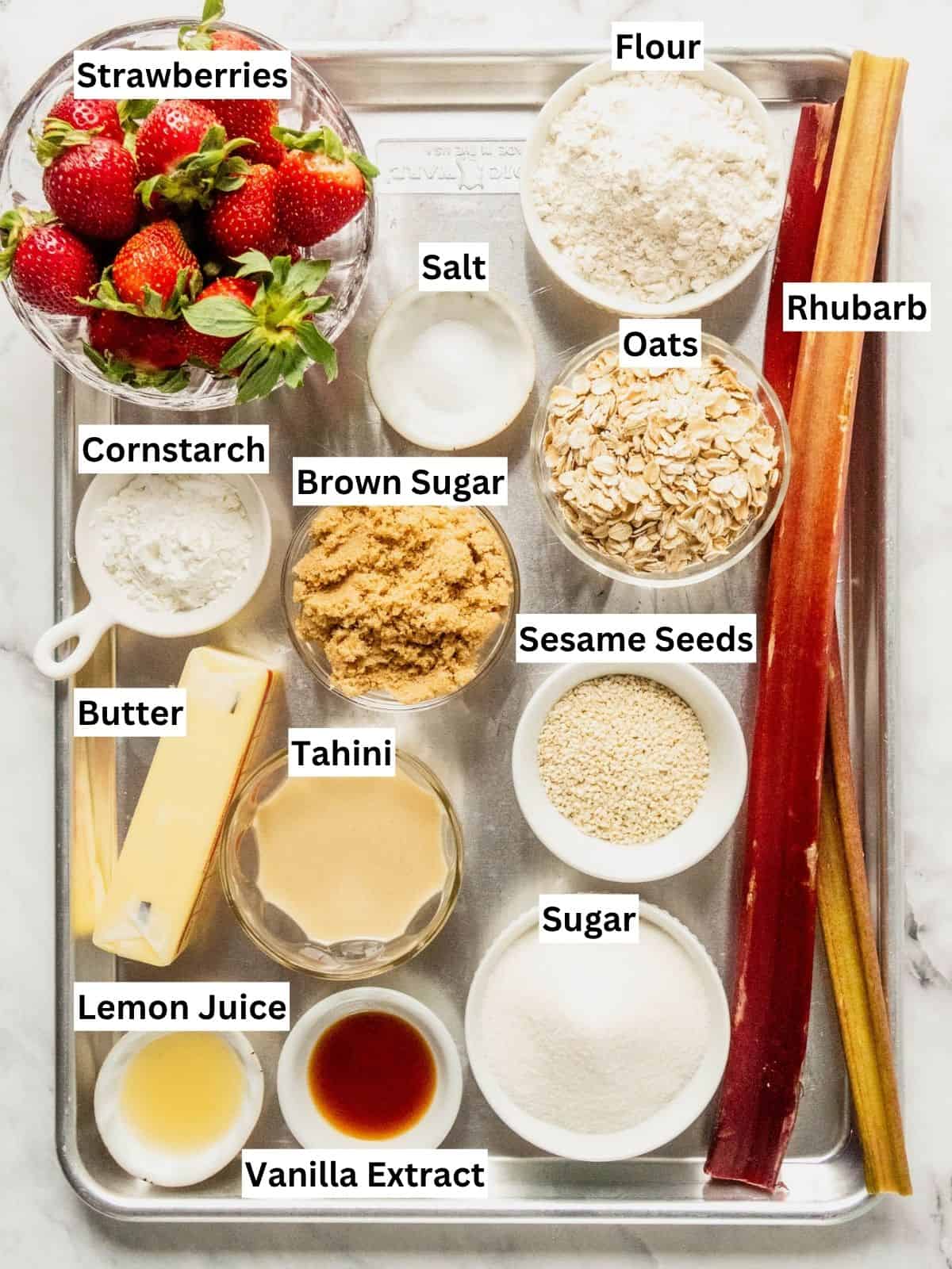Strawberry rhubarb crisp recipe ingredients with individual labels on a metal tray.