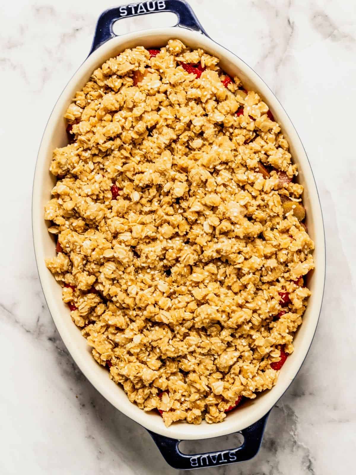 Layering the crisp topping on top of the fruit mixture in an oval baking dish.