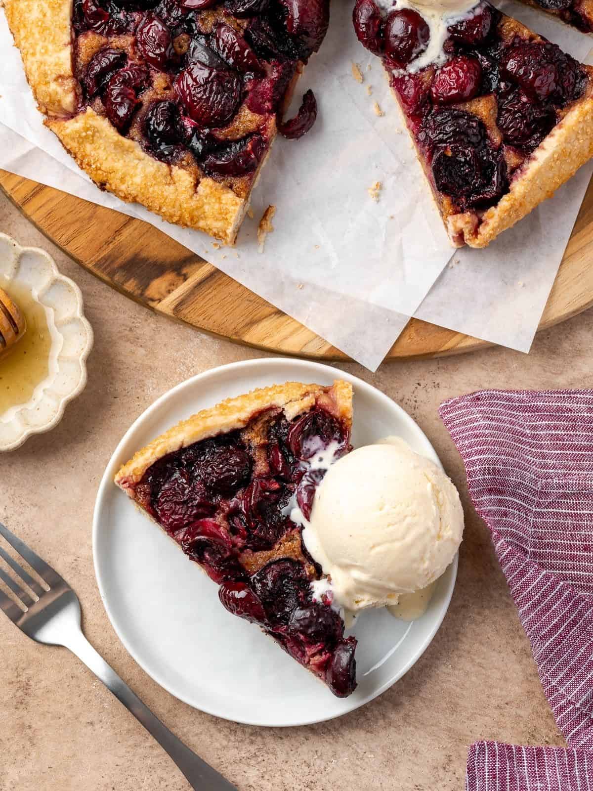 A slice of cherry galette with walnut frangipane with a scoop of ice cream on the side.