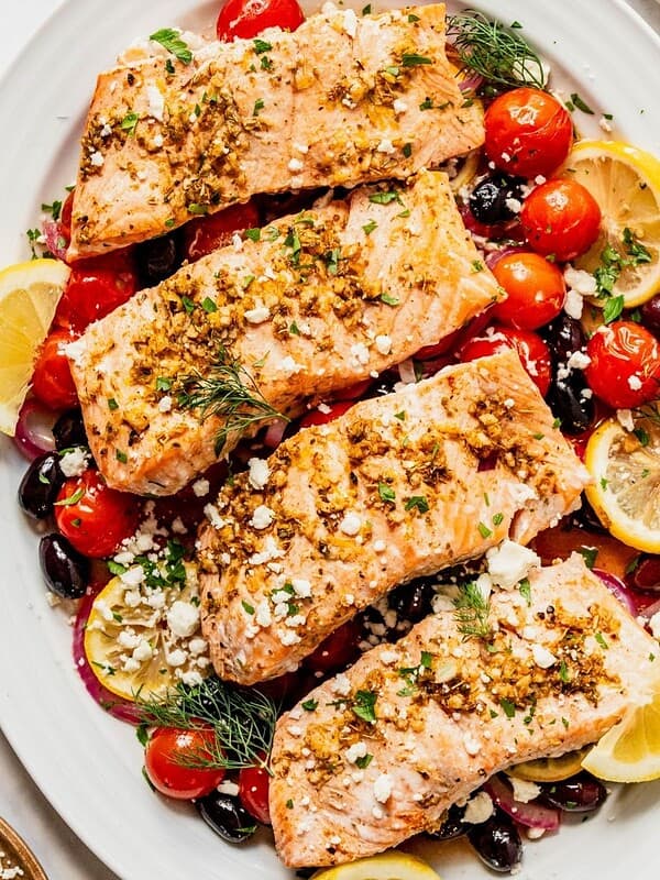 Greek salmon filets on a bed of cherry tomatoes, olives, onion, and lemon.