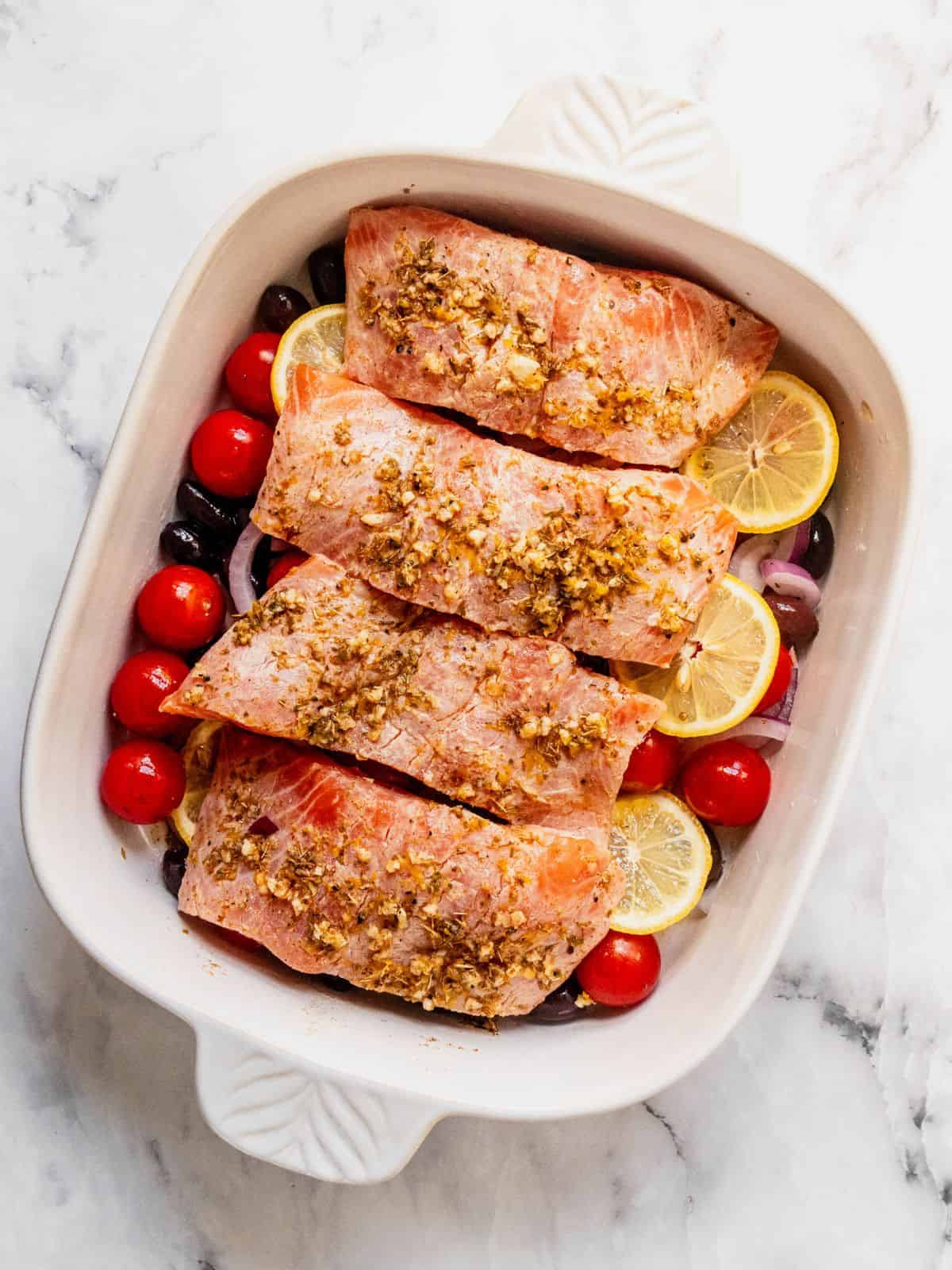 Seasoned filets of salmon placed over the sliced onion, lemon, cherry tomatoes and olives.
