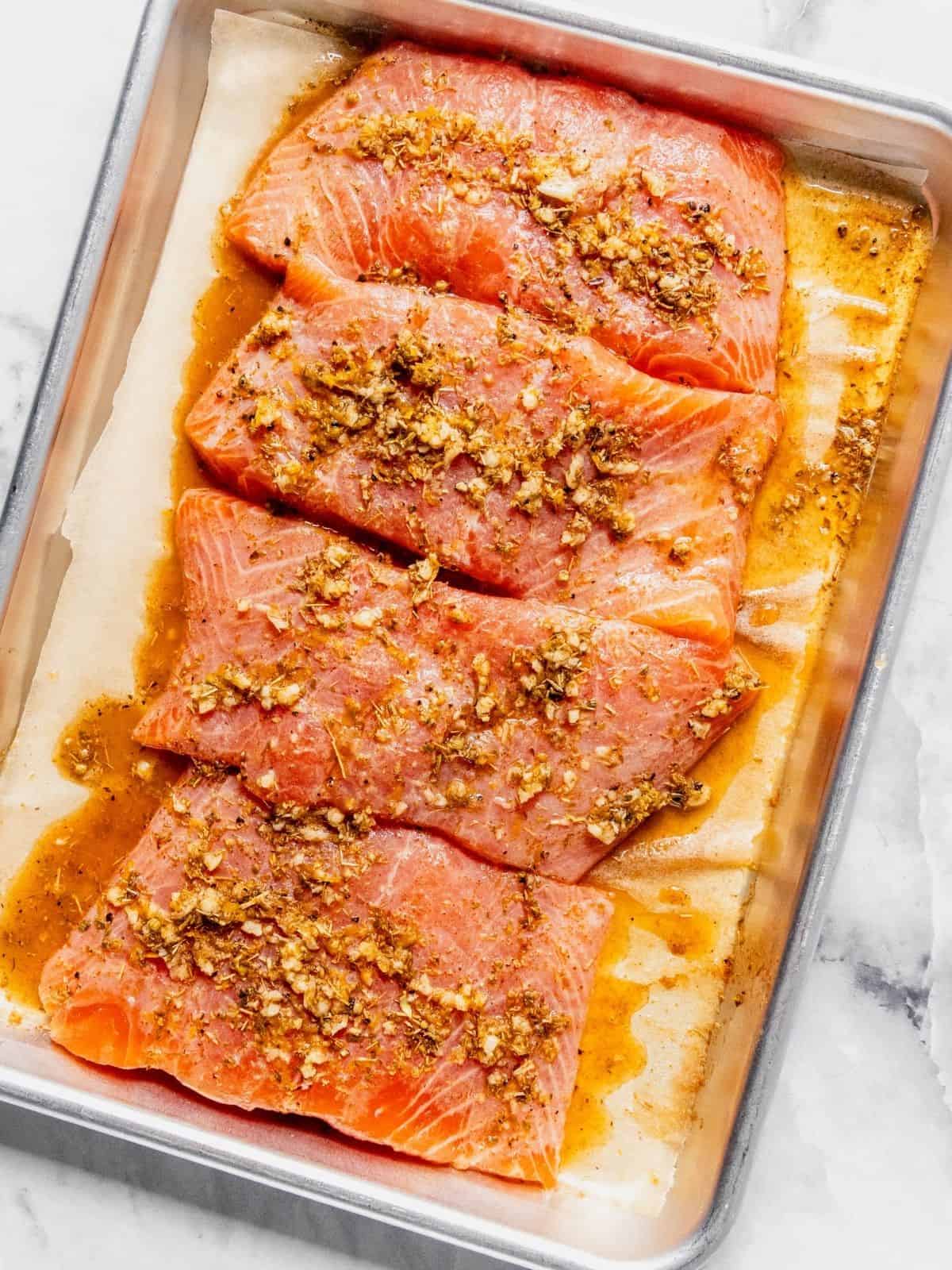 Rimmed baking sheet with 4 salmon filets dressed in olive oil, spices and garlic.