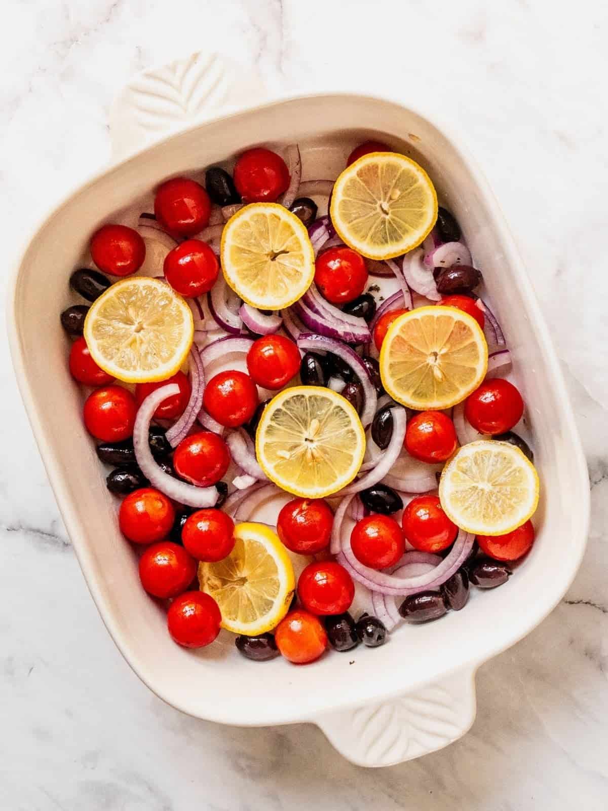 Baking tray with sliced lemons, onion, cherry tomatoes and olives.