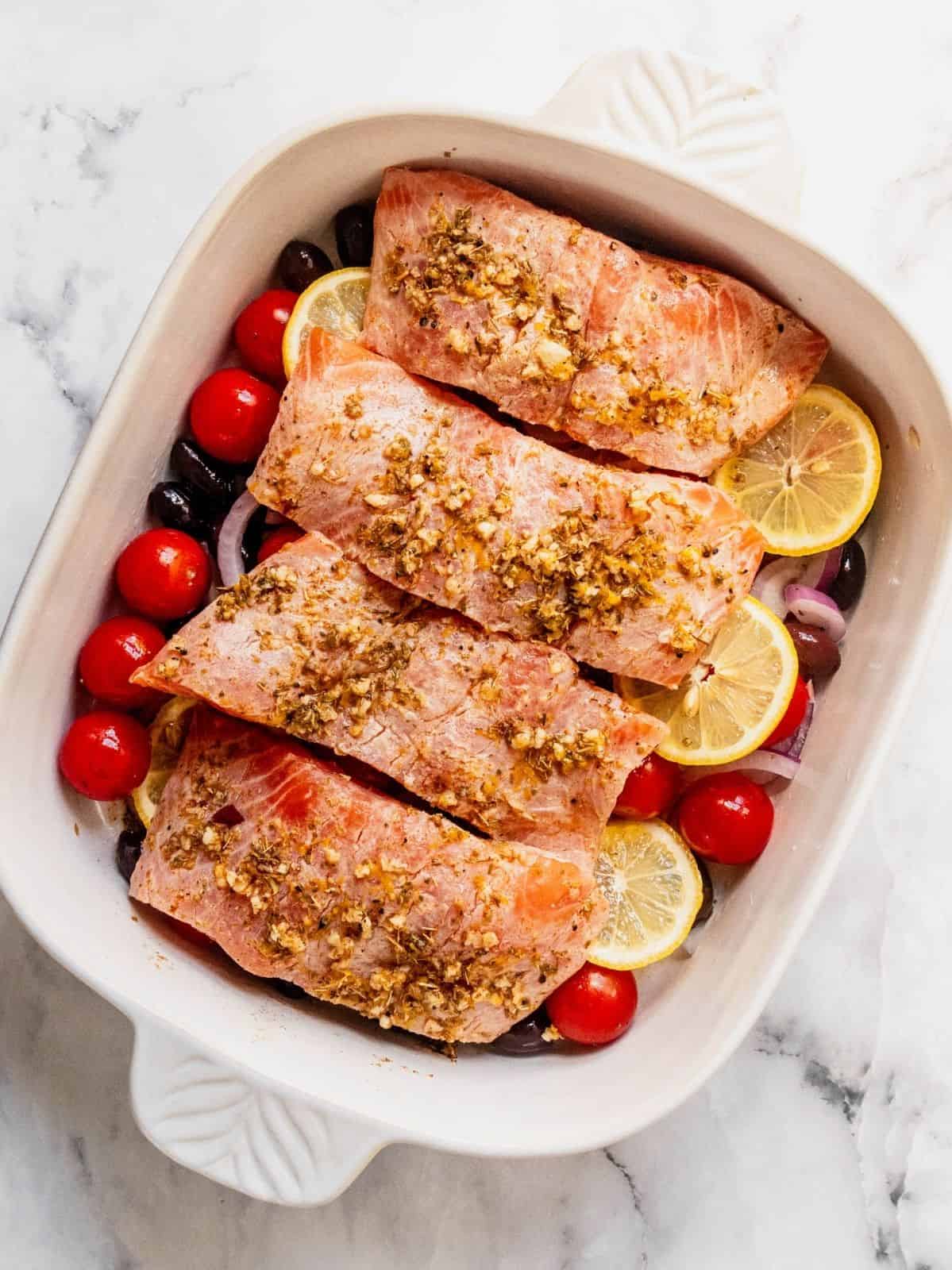 Seasoned filets of salmon placed over the sliced onion, lemon, cherry tomatoes and olives.