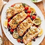 Greek salmon filets on a bed of cherry tomatoes, olives, onion, and lemon.