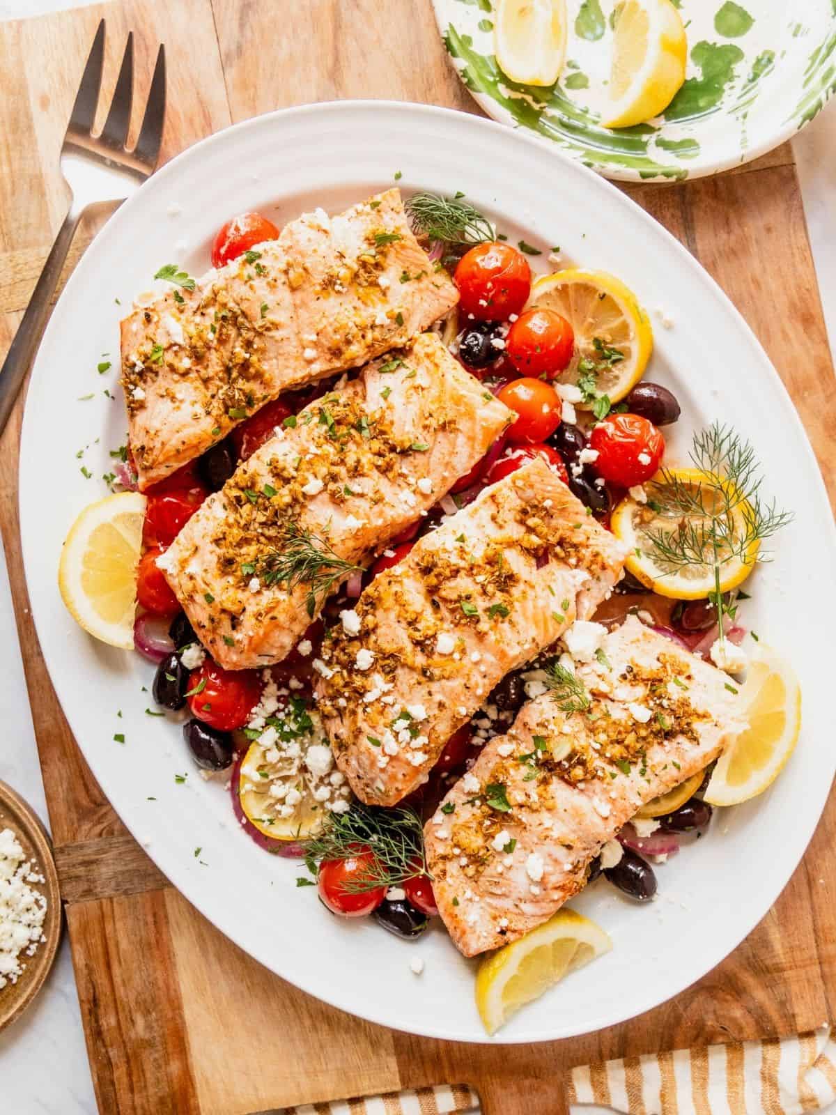 Greek salmon filets on a bed of cherry tomatoes, olives, onion, and lemon.