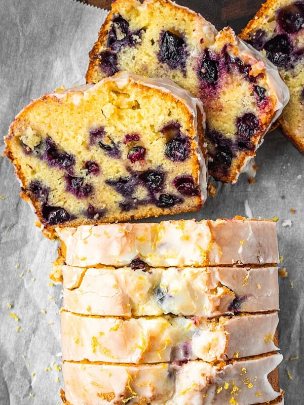 Lemon blueberry loaf slices with lemon icing on parchment paper.