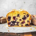 Blueberry lemon loaf slices with lemon icing on parchment paper.