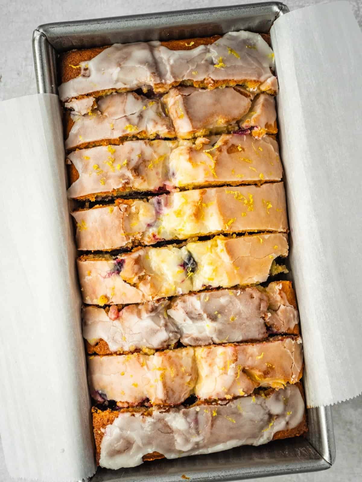 Lemon blueberry loaf slices with lemon icing on parchment paper in a loaf pan.
