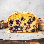 Blueberry lemon loaf slices with lemon icing on parchment paper.