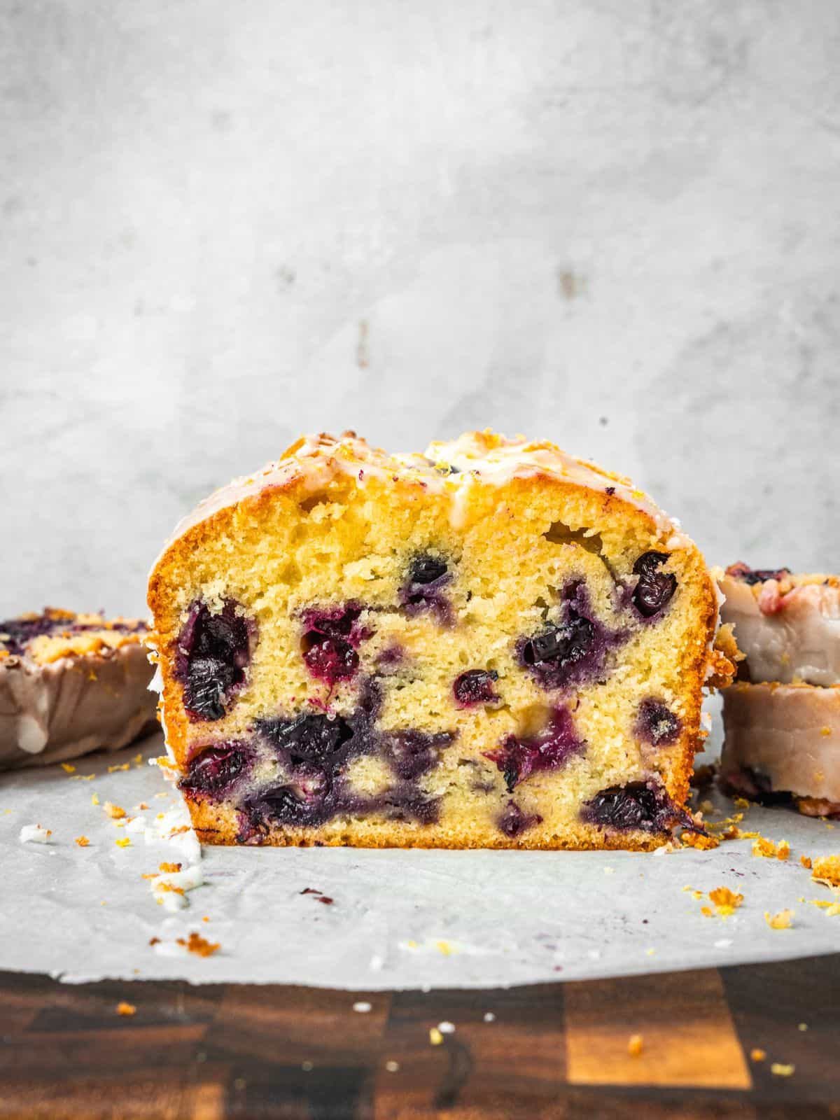 Blueberry lemon loaf slices with lemon icing on parchment paper.