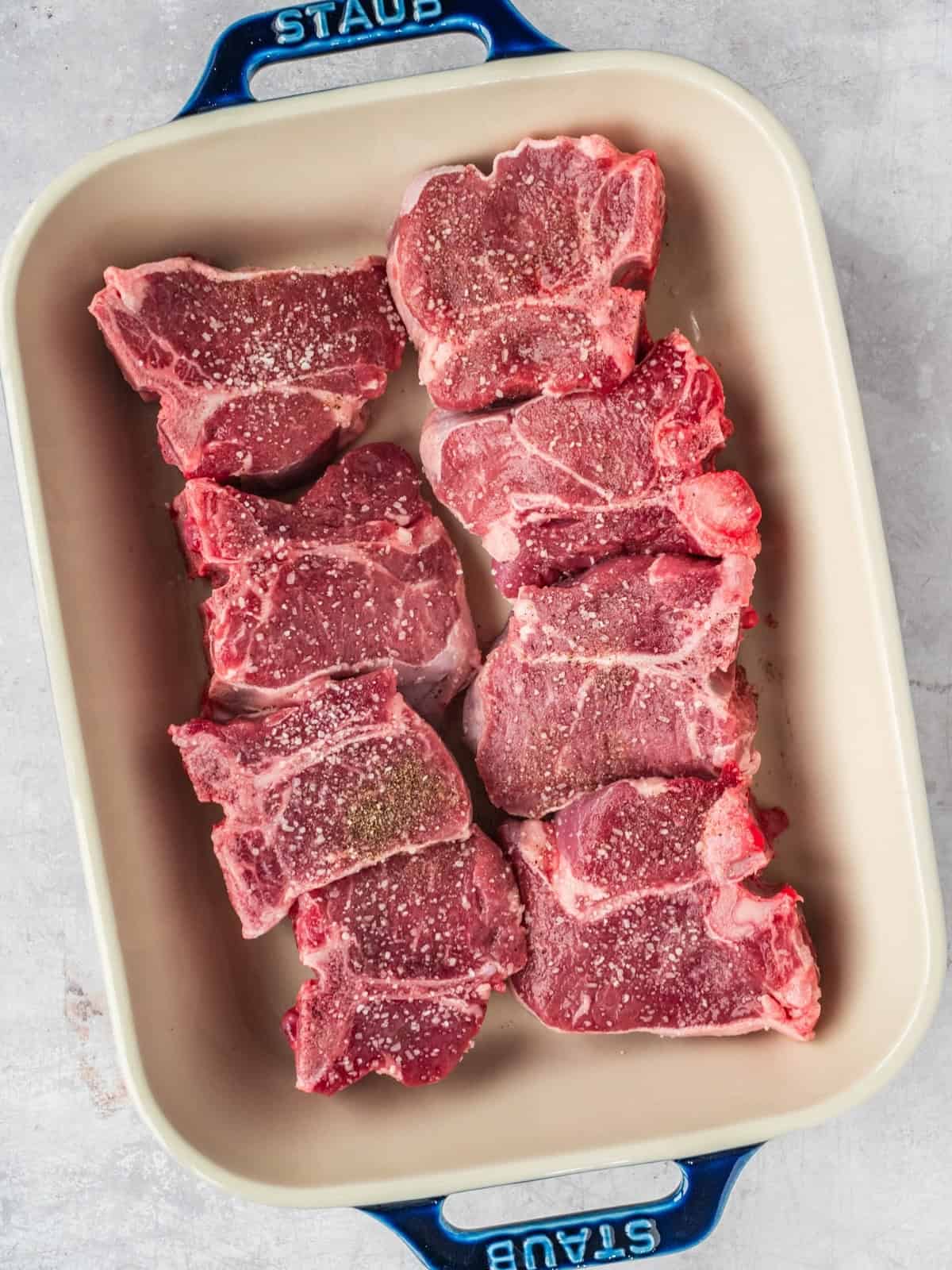 Lamb loin chops in a ceramic baking dish seasoned with salt, pepper and olive oil.