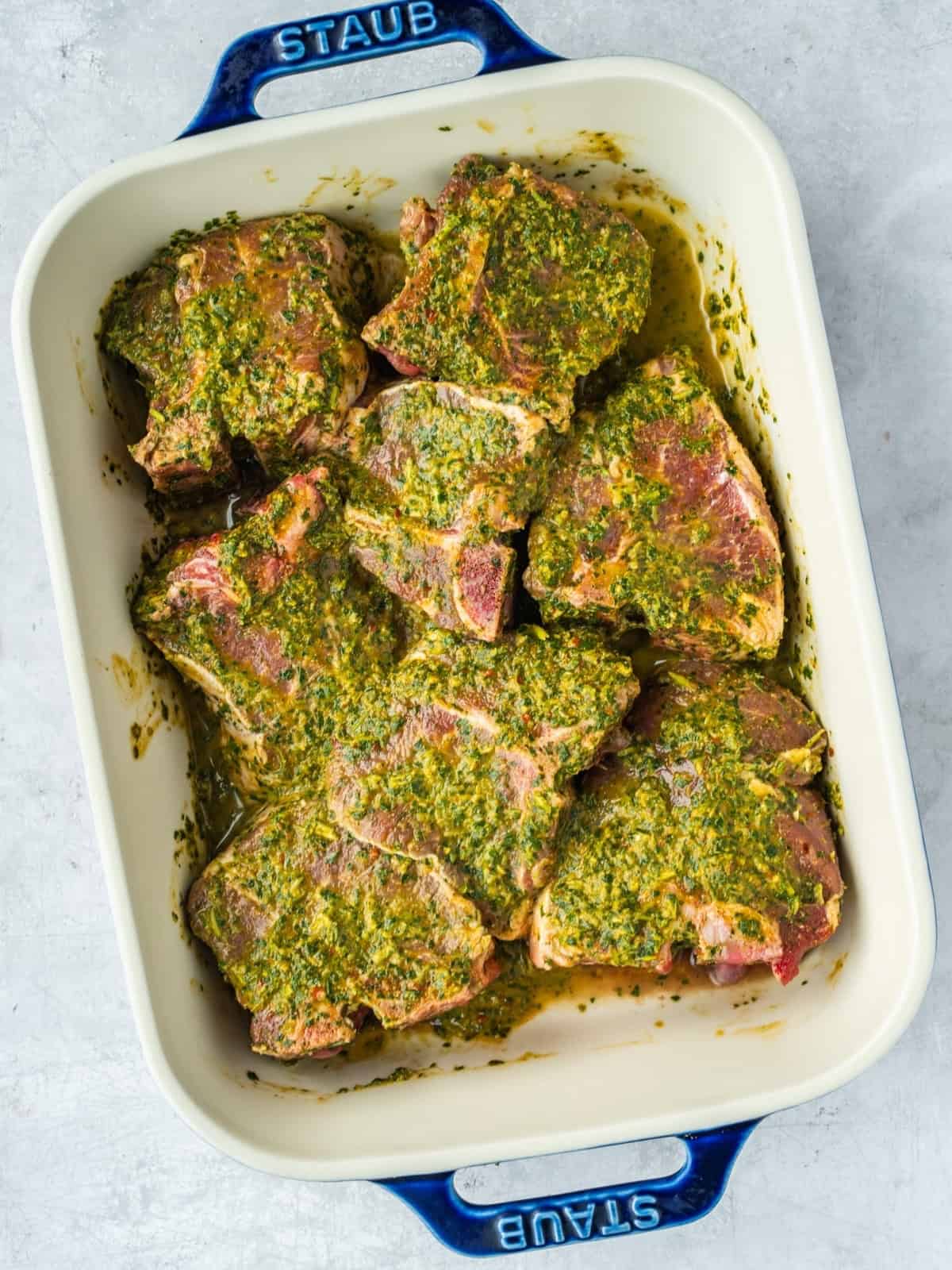 Lamb loin chops marinating in chermoula marinade in a ceramic baking dish.