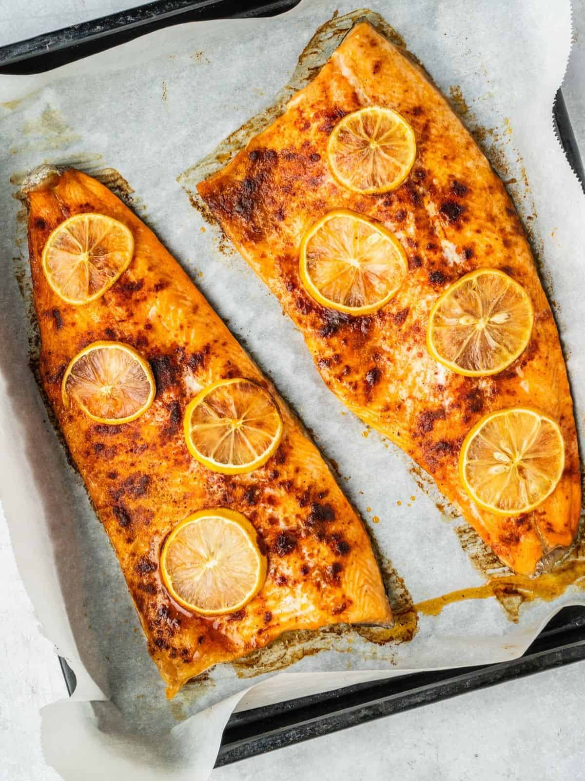 Baked trout fillets topped with lemon slices on a baking sheet.